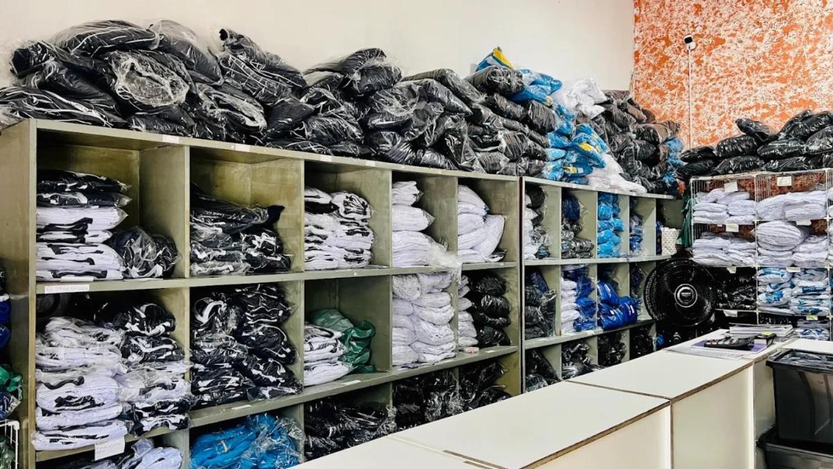 Interior da loja Daqfé: prateleiras cheias de uniformes embalados, separados por cor